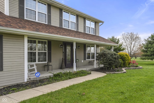 view of front of home featuring a front yard, a shingled roof, and covered porch