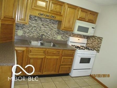 kitchen with tasteful backsplash, a sink, white appliances, and light tile patterned floors
