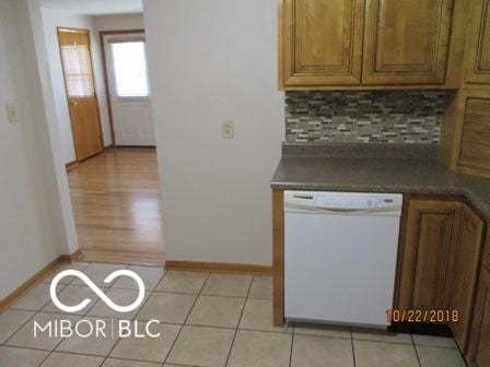 kitchen with backsplash, dark countertops, white dishwasher, baseboards, and brown cabinetry