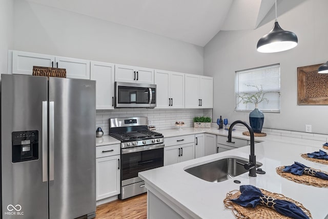 kitchen featuring white cabinets, a sink, light countertops, appliances with stainless steel finishes, and vaulted ceiling