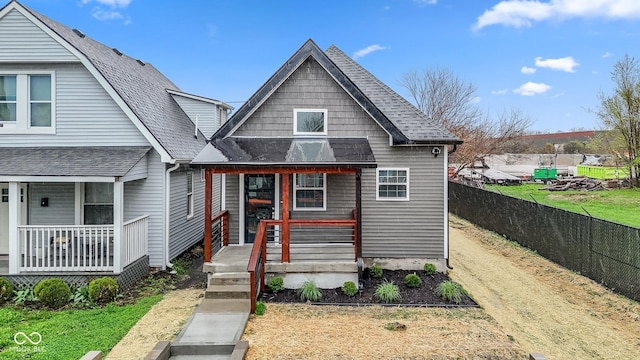 view of front facade with roof with shingles, fence, and covered porch
