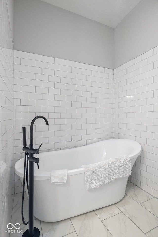 bathroom featuring marble finish floor, tile walls, and a soaking tub