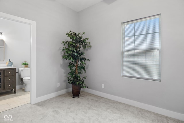bedroom with baseboards, connected bathroom, and light colored carpet