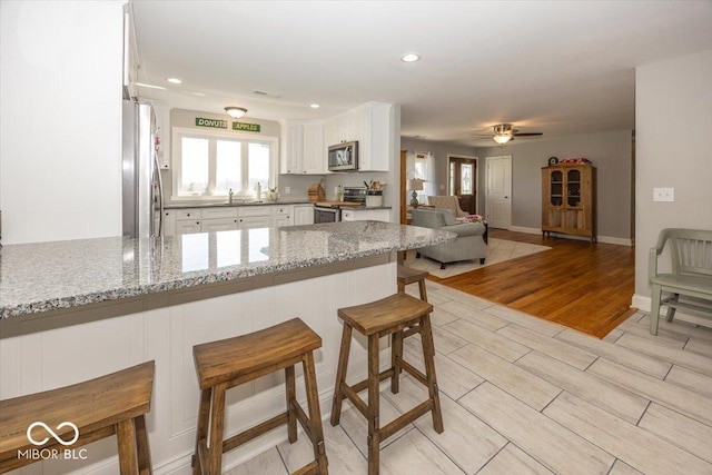 19702 Tomlinson Rd, Westfield, IN 46074 - kitchen featuring a peninsula, white cabinets, appliances with stainless steel finishes, light stone counters, and a sink