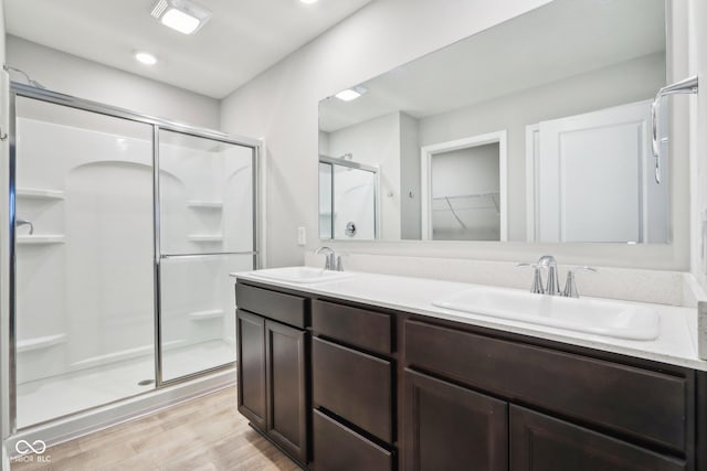 full bathroom with a sink, double vanity, a stall shower, and wood finished floors
