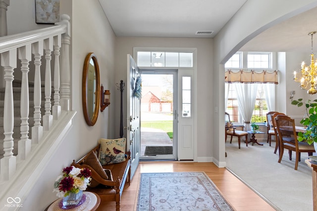 foyer entrance featuring arched walkways, light wood finished floors, visible vents, and an inviting chandelier