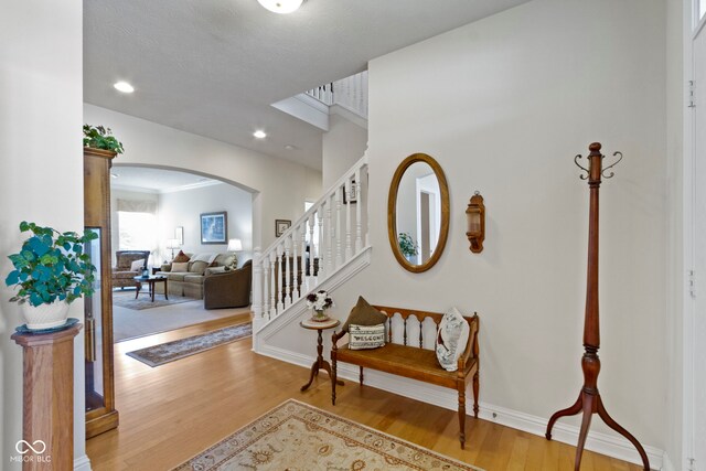 foyer with stairway, wood finished floors, arched walkways, baseboards, and recessed lighting