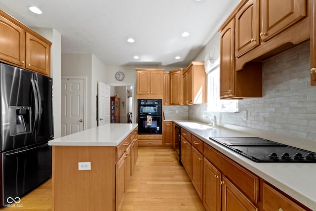 kitchen with light wood finished floors, a center island, tasteful backsplash, light countertops, and black appliances