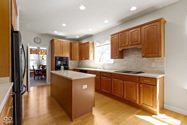 kitchen featuring light countertops, light wood-style flooring, decorative backsplash, and black appliances