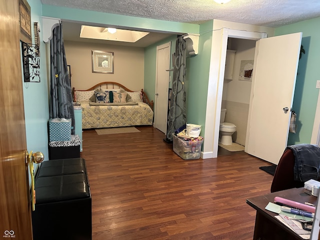 bedroom with ensuite bath, wood finished floors, and a textured ceiling