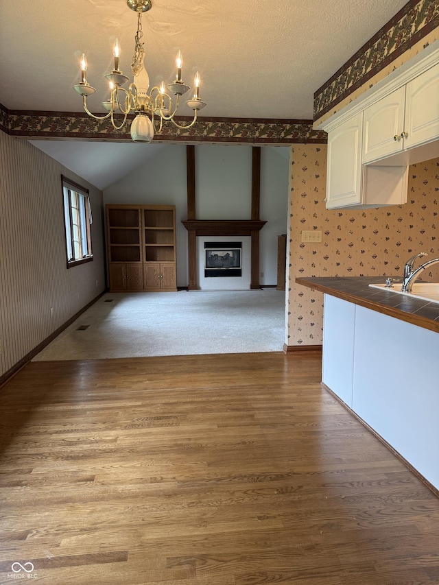 interior space with light wood-style floors, lofted ceiling, a notable chandelier, and wallpapered walls