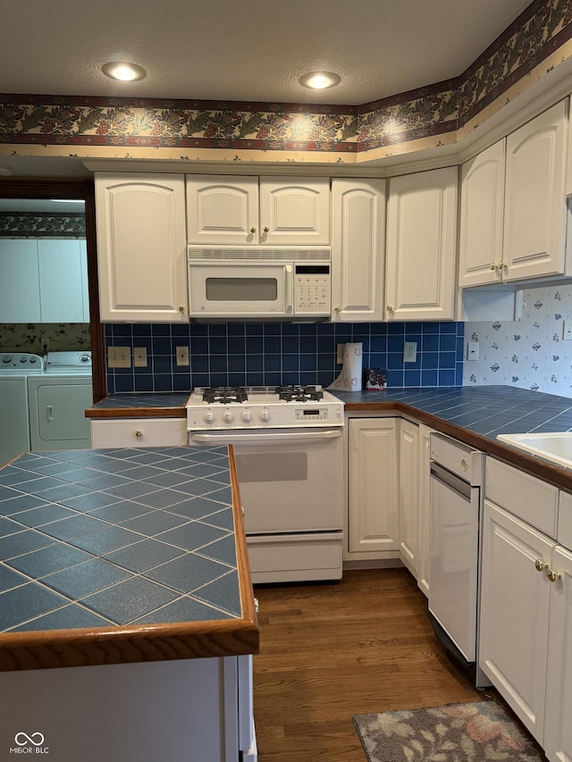kitchen with tile countertops, independent washer and dryer, white cabinets, and white appliances