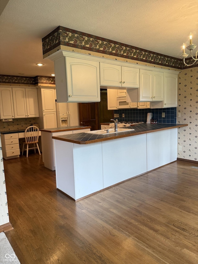 kitchen featuring an inviting chandelier, a textured ceiling, tile countertops, wallpapered walls, and dark wood-style floors
