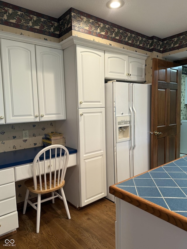 kitchen featuring built in desk, wallpapered walls, dark wood-style floors, and white refrigerator with ice dispenser