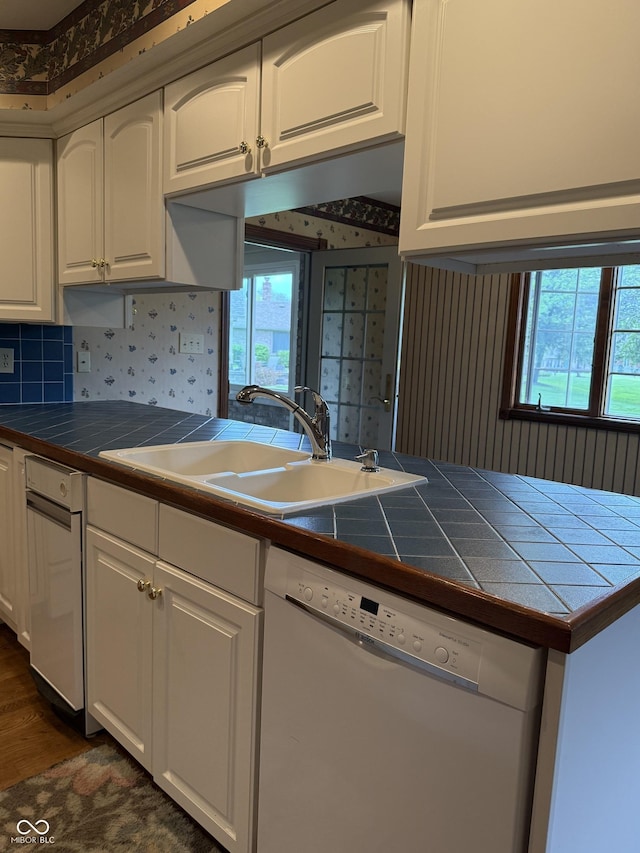 kitchen with white dishwasher, wallpapered walls, tile counters, a sink, and a wealth of natural light