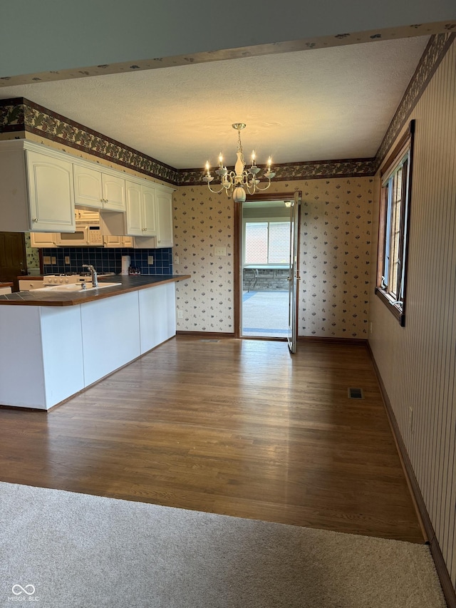 kitchen featuring dark countertops, an inviting chandelier, white cabinetry, wallpapered walls, and visible vents