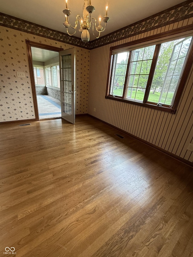 spare room featuring an inviting chandelier, wood finished floors, and wallpapered walls