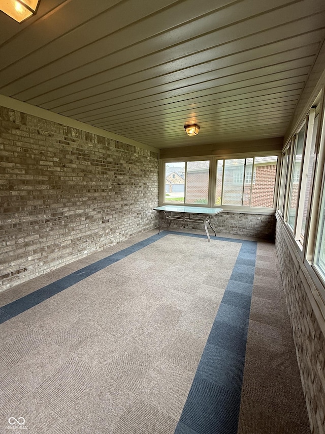 unfurnished sunroom featuring carpet flooring, wood ceiling, and brick wall