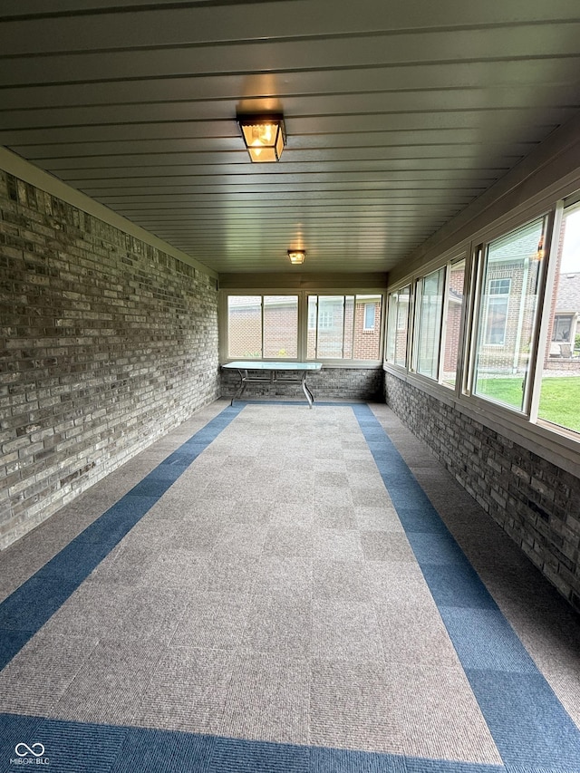 unfurnished sunroom with carpet flooring, brick wall, and plenty of natural light