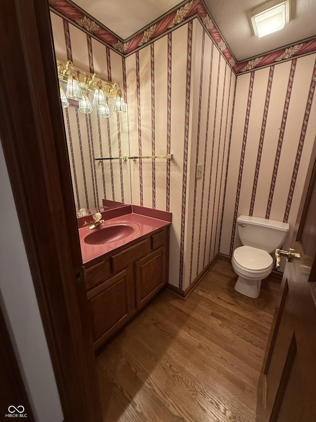 bathroom with vanity, wallpapered walls, toilet, and wood finished floors