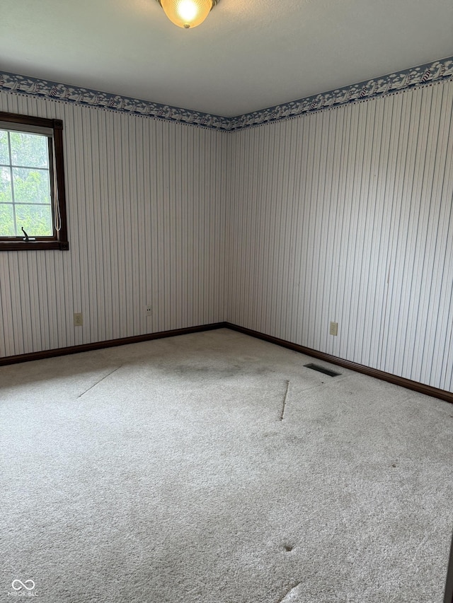 carpeted empty room featuring wallpapered walls and visible vents