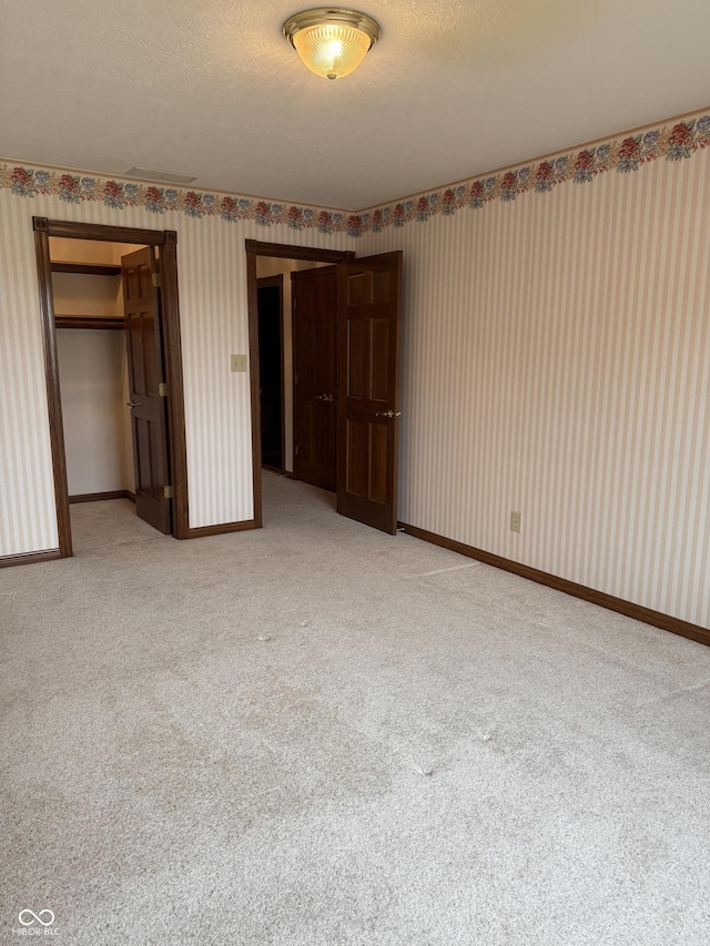 unfurnished bedroom with carpet flooring, wallpapered walls, baseboards, and a closet