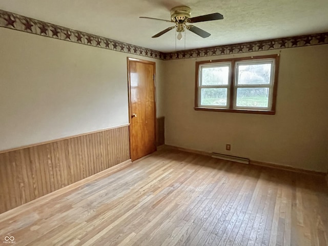 unfurnished room with ceiling fan, wainscoting, light wood-type flooring, baseboards, and wooden walls