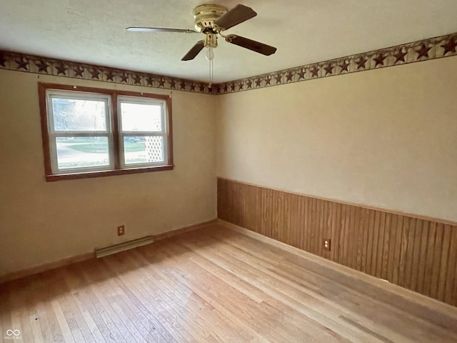empty room with ceiling fan, visible vents, light wood-style flooring, and a wainscoted wall