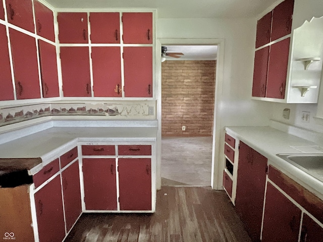 kitchen featuring a sink, red cabinetry, light countertops, a ceiling fan, and dark wood-type flooring