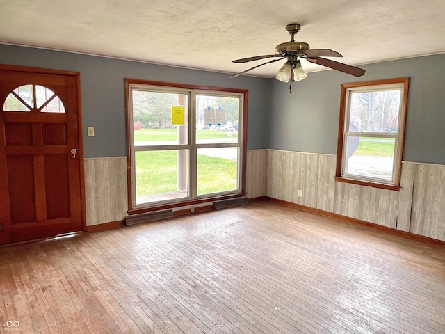 foyer entrance featuring wainscoting, wood walls, light wood-style flooring, and a wealth of natural light