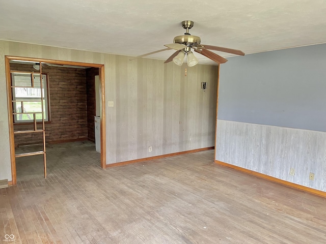spare room featuring a ceiling fan, baseboards, wood walls, and wood finished floors