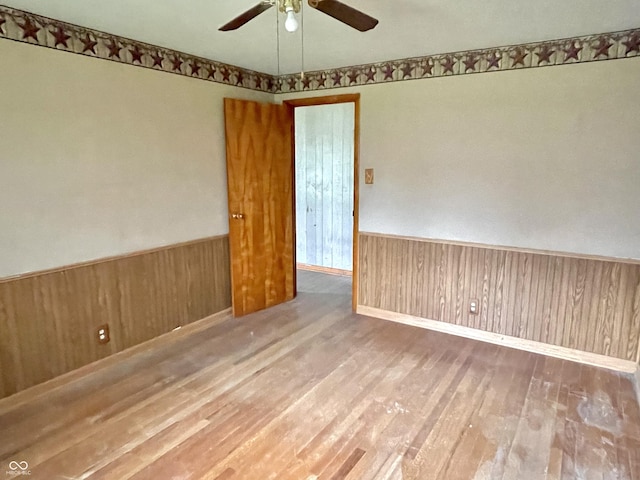 unfurnished room with wood walls, wainscoting, ceiling fan, and wood finished floors