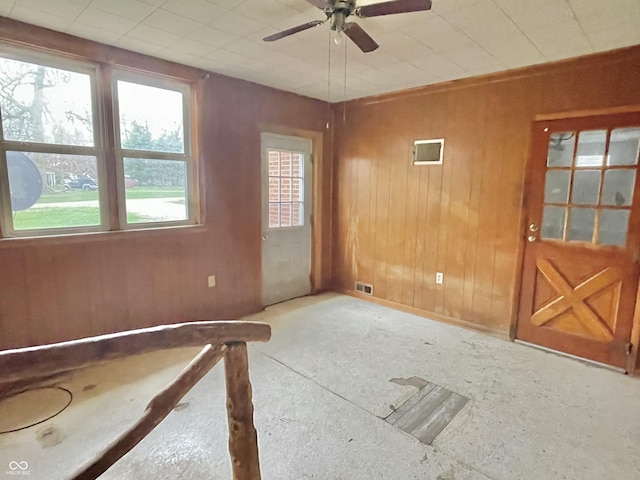 spare room with a ceiling fan, wood walls, and visible vents