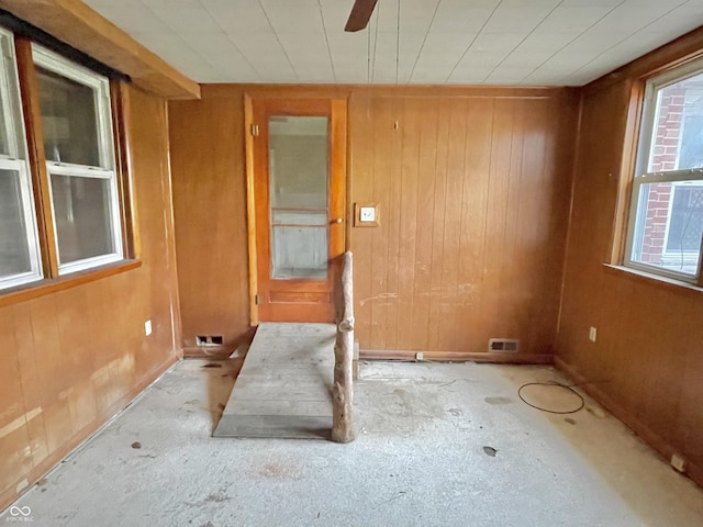 unfurnished room with baseboards, wood walls, a ceiling fan, and visible vents
