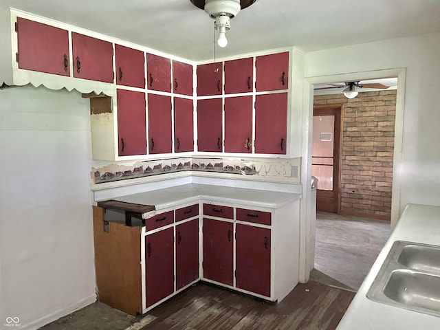 kitchen featuring a ceiling fan, dark wood-type flooring, red cabinets, light countertops, and a sink