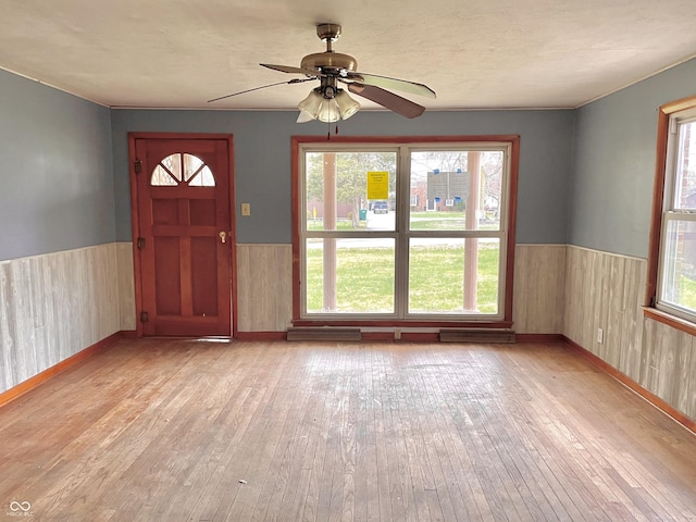 foyer featuring ceiling fan, wainscoting, wood walls, light wood-type flooring, and baseboards
