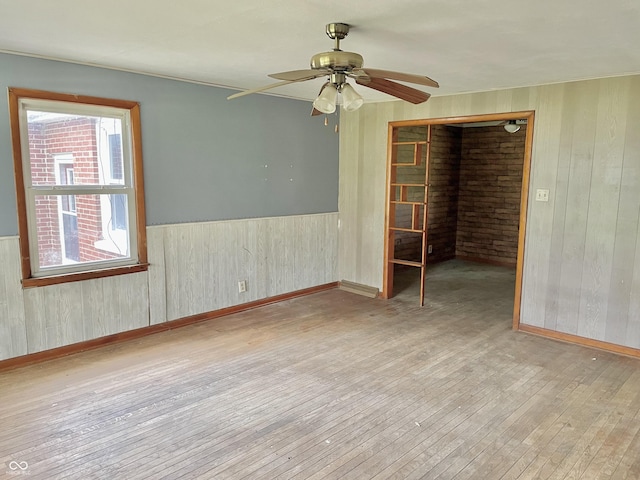 spare room featuring a wainscoted wall, wood-type flooring, a ceiling fan, and wood walls