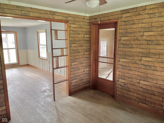 empty room featuring wooden walls, a wainscoted wall, ceiling fan, and wood-type flooring