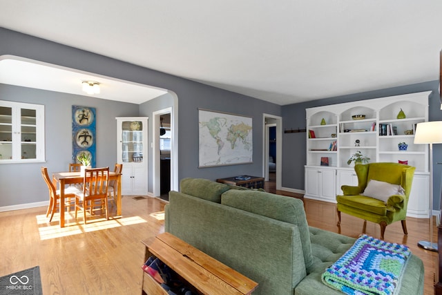 living room featuring arched walkways, baseboards, and light wood-style flooring