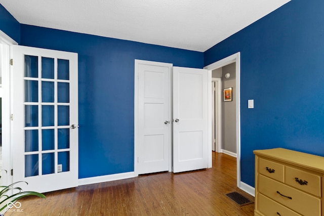 unfurnished bedroom featuring baseboards, wood finished floors, and visible vents