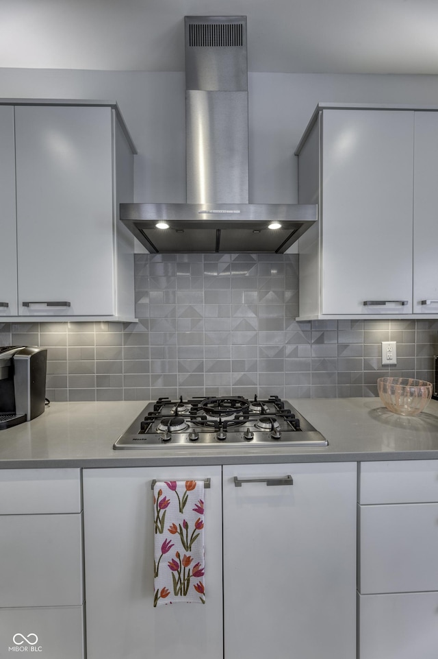 kitchen featuring wall chimney range hood, light countertops, white cabinets, and stainless steel gas stovetop