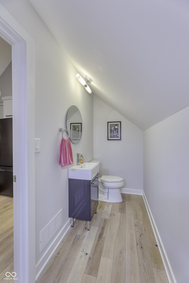 bathroom featuring vanity, toilet, wood finished floors, lofted ceiling, and visible vents