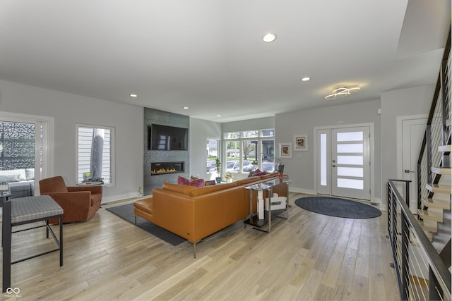 living room featuring stairs, recessed lighting, a tiled fireplace, and light wood-style flooring