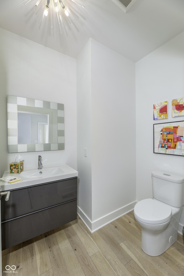 half bathroom featuring vanity, baseboards, toilet, and wood finished floors