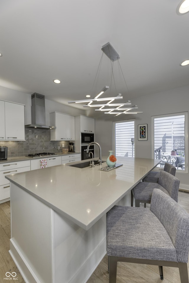 kitchen featuring wall chimney exhaust hood, appliances with stainless steel finishes, white cabinets, and tasteful backsplash