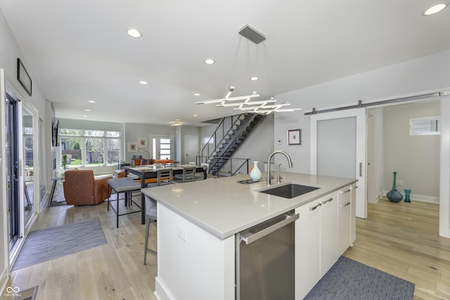 kitchen featuring an island with sink, a barn door, white cabinets, a sink, and dishwasher