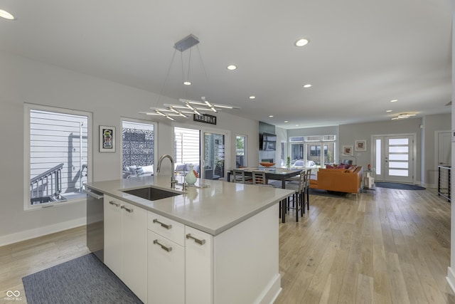 kitchen featuring plenty of natural light, light wood-style flooring, a sink, white cabinetry, and an island with sink