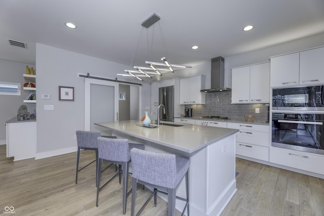 kitchen featuring appliances with stainless steel finishes, tasteful backsplash, a barn door, a sink, and wall chimney exhaust hood