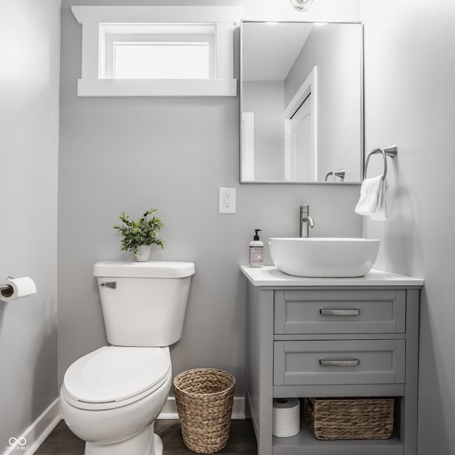 half bathroom featuring toilet, baseboards, wood finished floors, and vanity