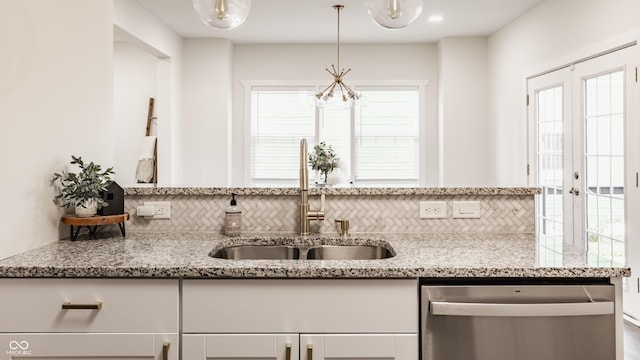 kitchen with light stone countertops, dishwasher, white cabinetry, a sink, and backsplash
